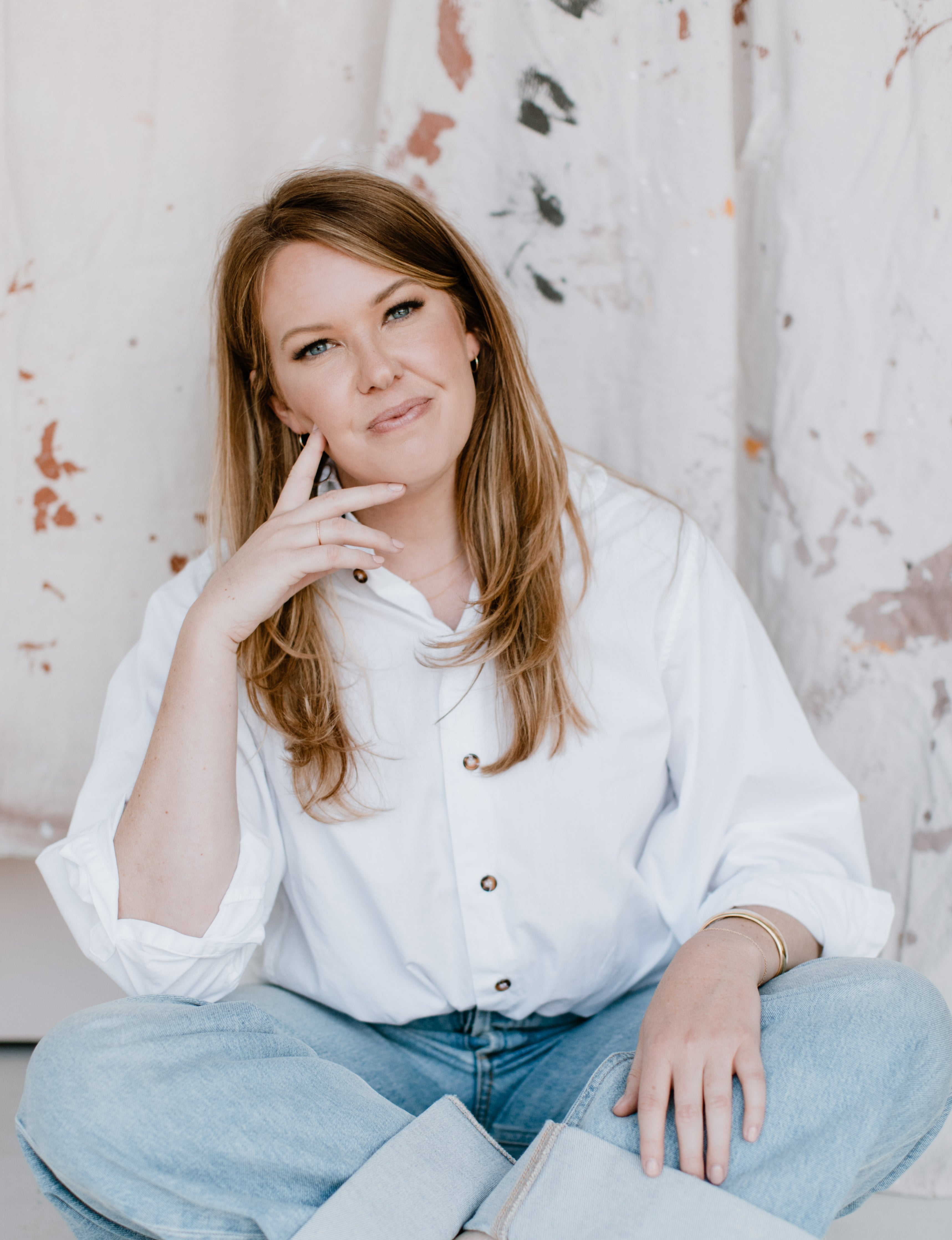 Laura, the Founder of Just Okay, sits among painting materials.